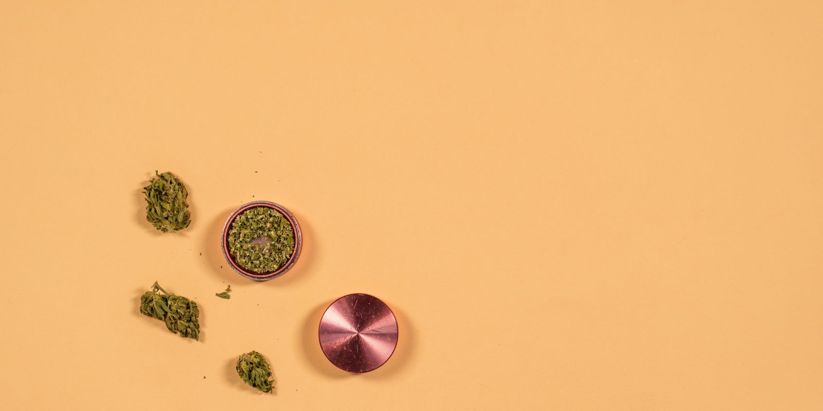 Photo vue du dessus d'un grinder en deux parties. La partie inférieure contient de la weed. De l'herbe est posée à côté.